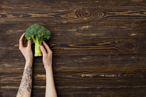 Overhead view of fresh broccoli in hands over wooden background