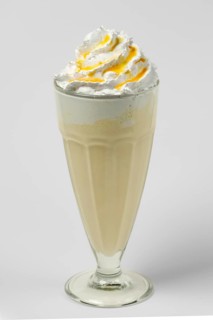 Mango and lemon milkshake summer cocktail in tall facetted glass on gray background