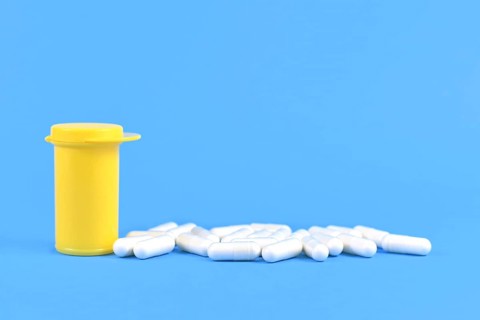 Capsule pills next to yellow medicine container on bright blue background