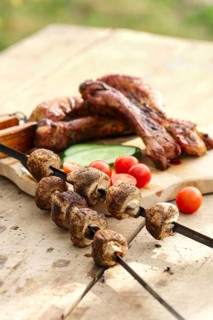 Grilled ribs and champignon on skewer served with fresh cucumber and tomato on wooden table outdoor