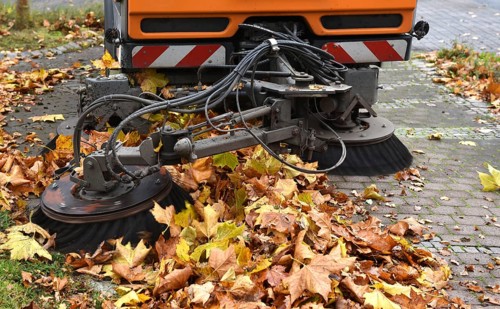 Sweeper sweeps up wilted leaves in autumn