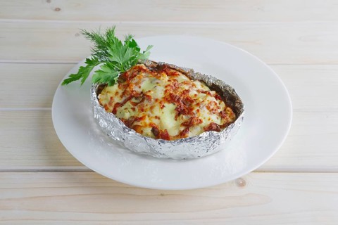 Meat baked in foil with vegetables and cheese on wooden table