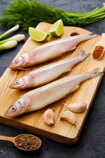 Raw fresh smelt fish on wooden cutting board with spice and herbs