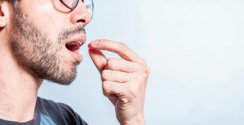 Man putting a pill in his mouth isolated. Close-up of a man taking an aspirin. Person taking a pill isolated