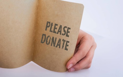 Hand holding a sheet of paper with please donate wording