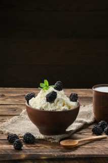 Dairy product cottage cheese and milk in brown ceramic bowl with spoon on wooden table
