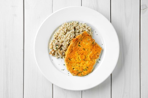 Top view of schnitzel with green buckwheat on white wooden table