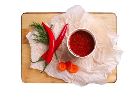 Top view of plate with hot and spicy soup with chilli pepper and carrot isolated on white