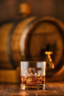 Glass of whisky with ice with barrel on background