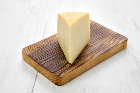 Triangular piece of goat cheese on wooden cutting board on black background