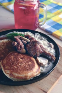 Fried in oven rabbit with fritters and onion sauce. Cast iron pan on wooden cutting board and glass with cranberry juice