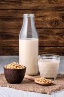 Bottle of soy milk with soybeans on white table over dark wooden background