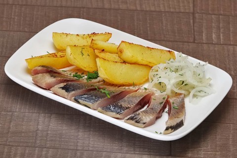 Plate with pickled herring and onion with potato wedges on wooden table