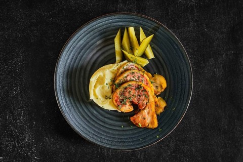 Top view of baked bacon with mashed potato and pickle cucumber