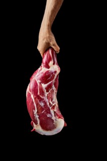 Hand of a butcher holds raw leg of lamb over black background