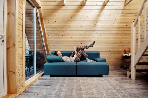 Middle aged man relaxing with book on sofa at chalet. Man in checkered trousers