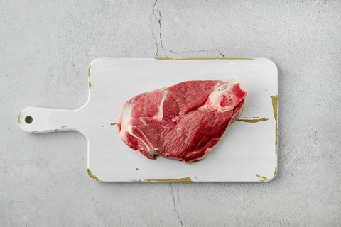 Top view of raw lamb leg cut as a steak. Slice of shank on white cutting board