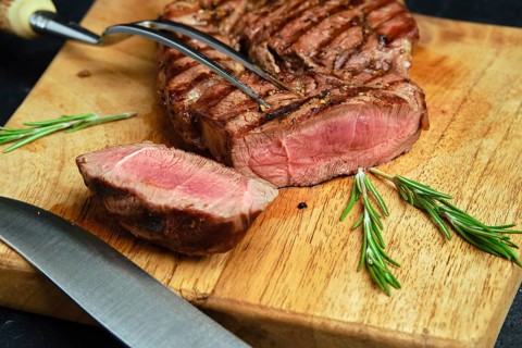 Close up view of juicy steak on wooden cutting board over black background