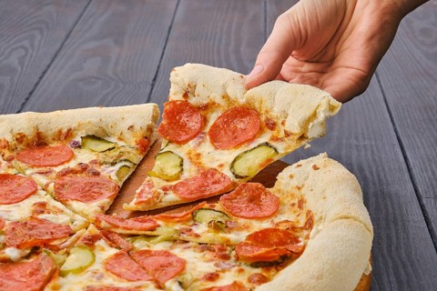 Hand taking slice of pizza pepperoni from plate