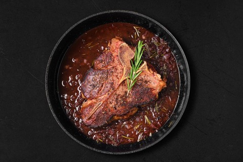 Overhead view of porterhouse steak in wine sauce in frying pan