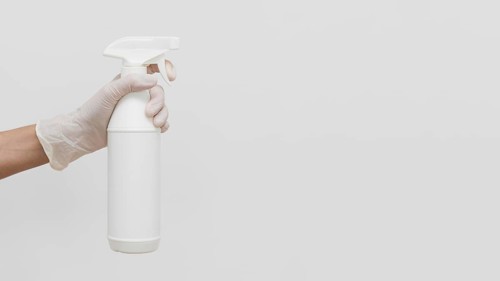 Hand with glove holding cleaning solution in bottle with copy space