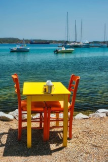 Yellow cafe restaurant table of street cafe with chairs on beach in Adamantas town on Milos island with Aegean sea with boats and yachts in background. Milos island