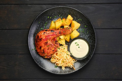 Top view of whole roasted chicken thigh with potato wedges and pickled cabbage