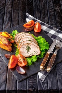 Sliced baked ham with fresh tomatoes on a stone plate in a rustic style