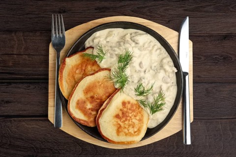 Flapjack with mushroom sauce on wooden plate. Top view