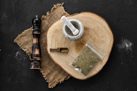Wooden cross section with Provencal herbs in plastic package and stone mortar and mill