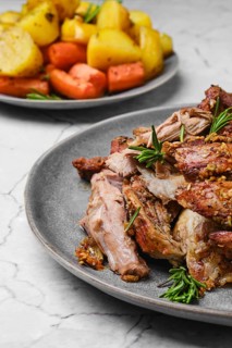 Closeup view of pulled lamb shoulder meat baked in oven with potato and carrot on marble table