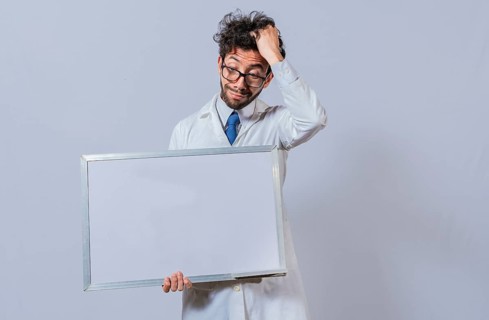 Male scientist in white coat holding and pointing at a blank whiteboard. Disheveled-haired man holding blank whiteboard