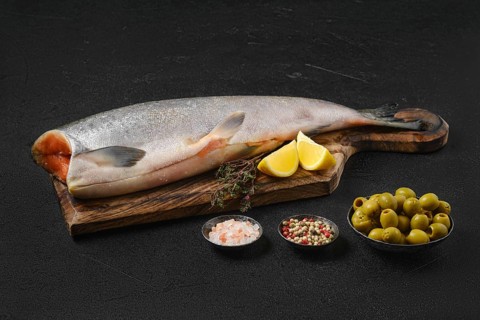 Headless fresh chinook on wooden cutting board with spice and lemon