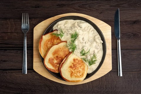 Flapjack with mushroom sauce on wooden plate. Top view