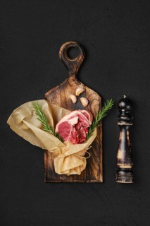 Raw fresh lamb double loin chop wrapped in paper on wooden cutting board