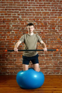 Athletic man doing exercises for the balance on rubber ball with gymnastic stick. Fitness workout