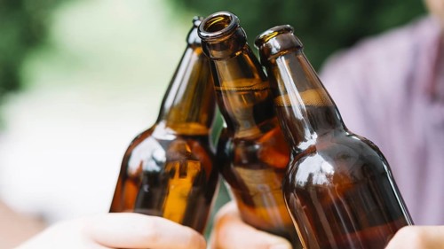 Close up friends clinking brown beer bottles
