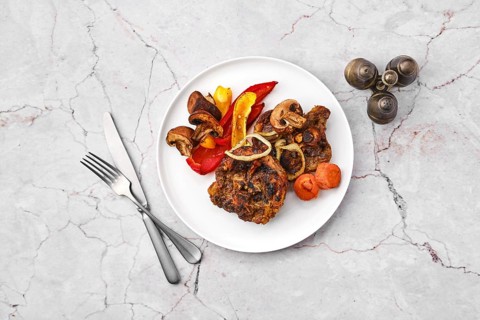 Overhead view of lamb neck with champignon and vegetables baked in oven on a plate