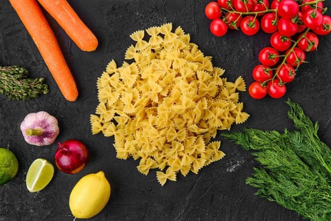 Overhead view of raw farfalle pasta with spice and herbs on black background