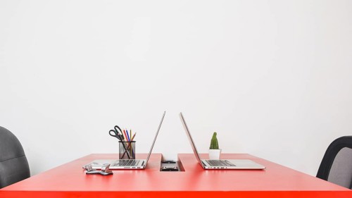 Modern workplace with two laptops red table against white wall