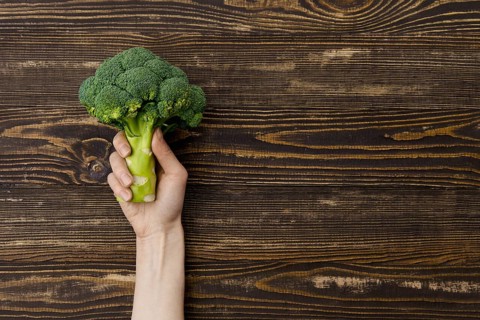 Overhead view of fresh broccoli in hands over wooden background