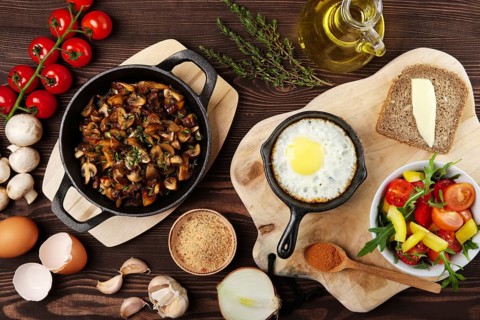 Vegetarian food. Fried mushrooms and egg in cast iron pan. Ingredients for rustic breakfast on wooden table