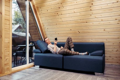 Man rests on sofa with smartphone in his forest cabin