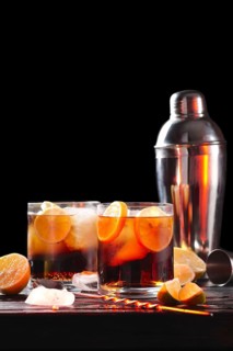 Selective focus composition with rum and cola cocktail served with citrus on rough paper and fabrick over the wooden table with pieces of ice