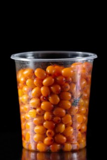 Plastic glass full of sea buckthorn on black background