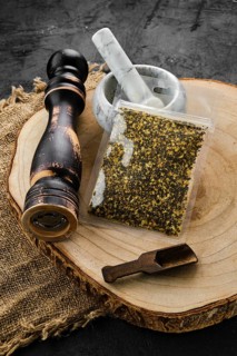 Wooden cross section with lemon pepper in plastic package and stone mortar and mill