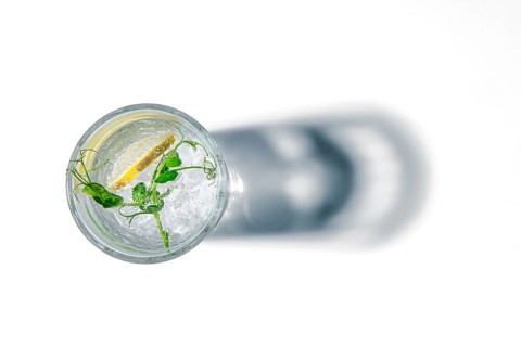 Overhead view of glass with cold water with ice and lemon casting a shadow on white background