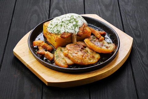 Potato casserole with fried pork mini belly slices on dark wooden table