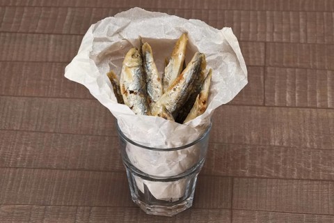 Fried sprat in rough facetted glass in wrapping paper on wooden table