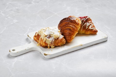 Assortment of fresh croissants on white serving board on marble background